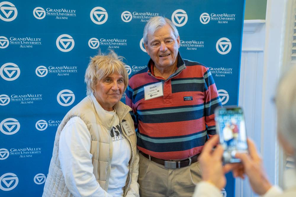 Two alumni getting their picture taken in front of the photo wall.